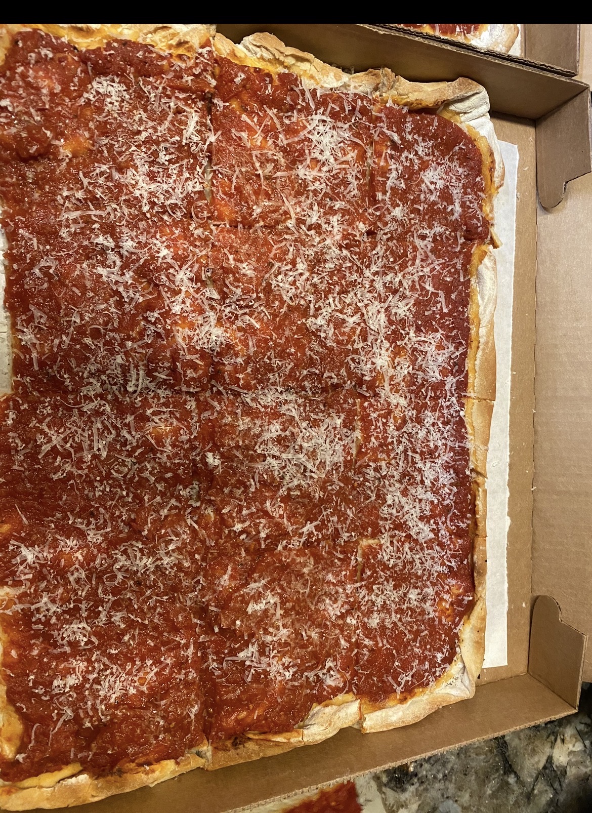 Sheet-pan Philadelphia tomato pie cut into squares, thick red sauce topped with grated cheese, in a bakery box