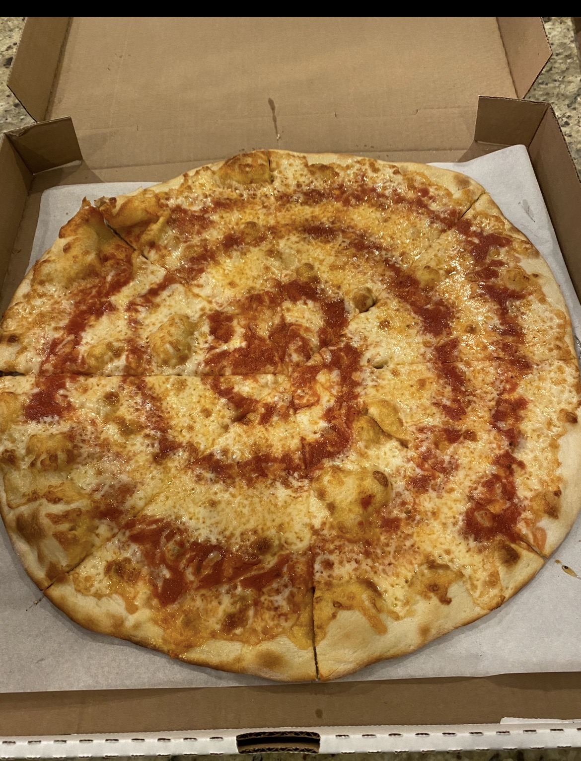 Whole round cheese pizza with swirled tomato sauce over melted mozzarella, sitting on paper in an open cardboard box