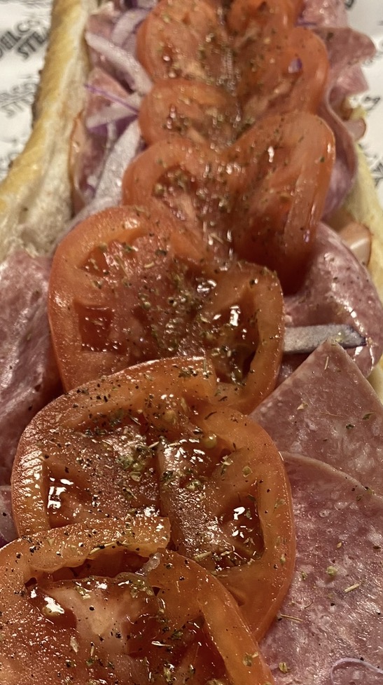 Open Italian hoagie layered with ham, salami, onion, tomato slices and oregano on a long roll